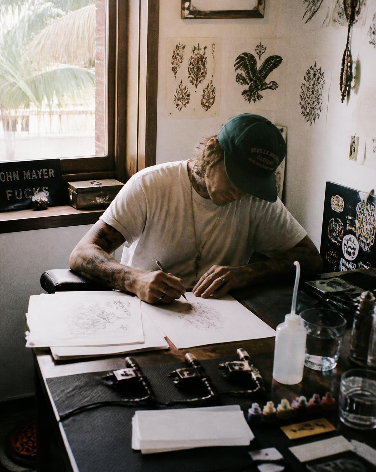 Tattoo artist sketching designs at a desk in a small studio