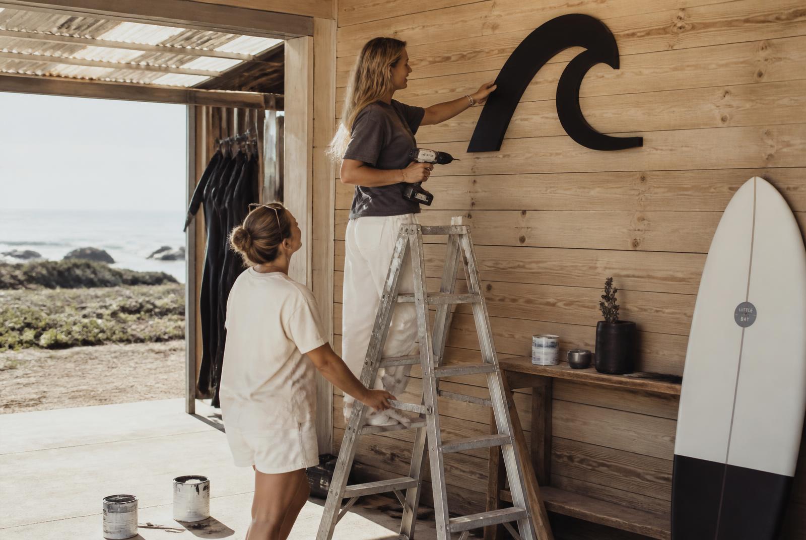 Women installing the New Wave wave symbol on a coastal workshop wall